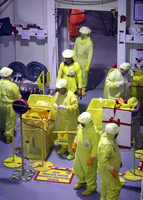 (Steve Ringman) A worker, top, checks a gauge in the Columbia Generating Station control room that shows the status of the fuel core. Below, workers on a shift change at the plant near Richland remove their protective clothing before moving outside the roped-off containment area.